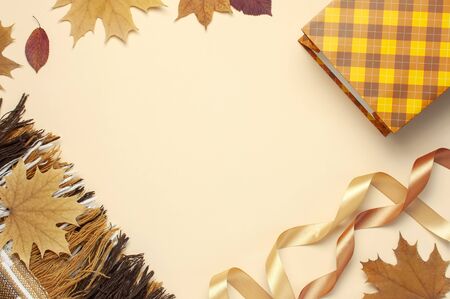 Autumn, fall concept. Checked orange gift paper bag, warm cozy blanket plaid, autumn dried leaves, holiday ribbons on pastel beige background. Flat lay top view copy space. Creative Autumn composition.の写真素材