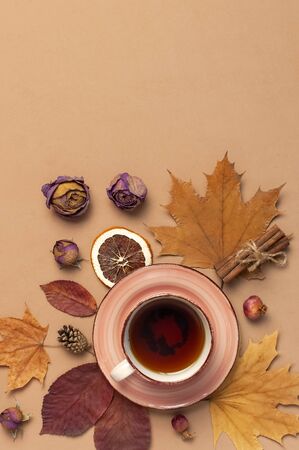 Autumn Flat lay composition. Cup of tea, autumn dry bright leaves, roses flowers, orange circle, cones, decorative pomegranate, cinnamon sticks on brown beige background top view. Autumn, fall concept.の写真素材