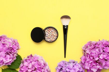 Set of decorative cosmetics makeup brushes, blush face balls, pink hydrangea flowers on yellow background top view Flat lay copy space. Beauty blogger concept. Fashion background. Makeup accessories.の写真素材