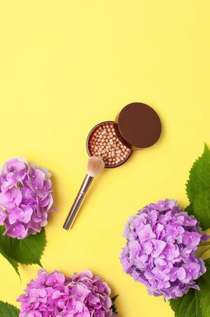 Set of decorative cosmetics makeup brushes, blush face balls, pink hydrangea flowers on yellow background top view Flat lay copy space. Beauty blogger concept. Fashion background. Makeup accessories.の写真素材