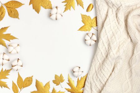 Flat lay autumn composition. Knitted woolen light beige sweater or plaid, golden dry leaves, cotton flowers on white background top view copy space. Autumn, fall concept.の写真素材