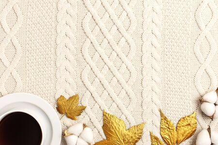 Flat lay autumn composition. Cup of coffee, knitted woolen light beige sweater or plaid, golden dry leaves, cotton flowers top view copy space. Autumn, fall concept. Cozy lifestyle details.の写真素材