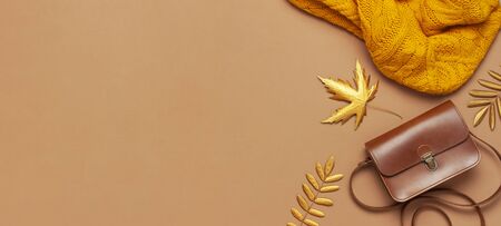 Brown leather women bag, orange knitted sweater, golden autumn leaf on brown background top view flat lay copy space. Fashionable women's accessories. Autumn Fashion Concept. Stylish Lady Clothes.の写真素材