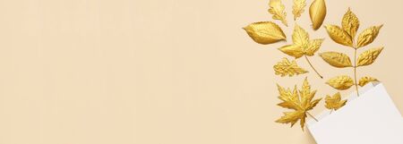 Flat lay creative autumn composition. White Gift Paper package and Golden leaves on beige background top view copy space. Fall concept. Autumn background. Minimal concept idea, floral design.の写真素材
