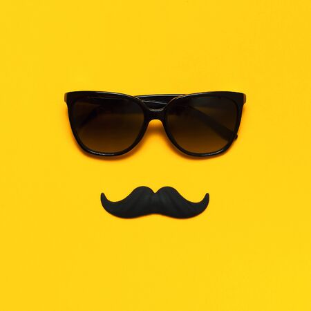 Creative party decoration concept. Black mustache, sunglasses, props for photo booths, carnival parties on yellow background top view flat lay copy space. Father's day Men's health awareness month.の写真素材