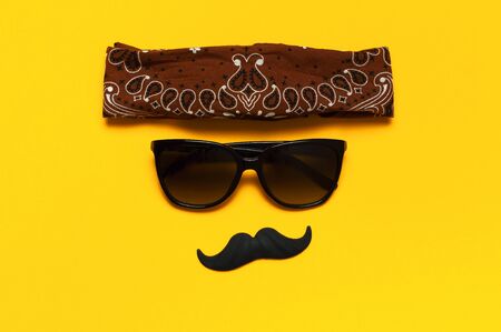 Creative party decoration concept. Black mustache, sunglasses, props for photo booths, carnival parties on yellow background top view flat lay copy space. Father's day Men's health awareness month.の写真素材