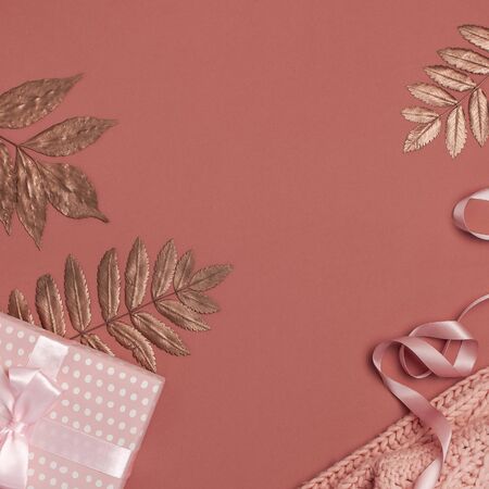 Flat lay autumn composition. Knitted woolen pink female sweater or plaid, pink gift with ribbon, golden dry leaves on burgundy brown background top view copy space. Autumn gift, fall concept.の写真素材