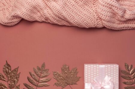 Flat lay autumn composition. Knitted woolen pink female sweater or plaid, pink gift with ribbon, golden dry leaves on burgundy brown background top view copy space. Autumn gift, fall concept.の写真素材