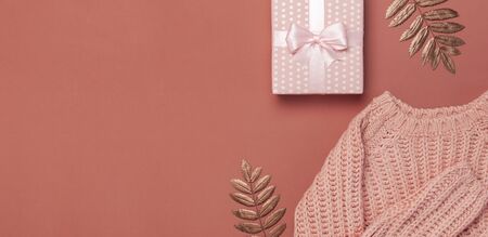 Flat lay autumn composition. Knitted woolen pink female sweater or plaid, pink gift with ribbon, golden dry leaves on burgundy brown background top view copy space. Autumn gift, fall concept.の写真素材