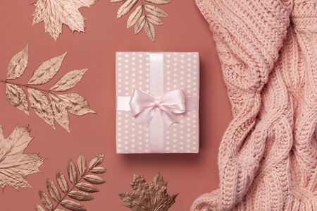 Flat lay autumn composition. Knitted woolen pink female sweater or plaid, pink gift with ribbon, golden dry leaves on burgundy brown background top view copy space. Autumn gift, fall concept.の写真素材