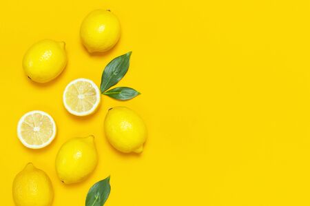 Ripe juicy lemons and green leaves on bright yellow background. Lemon fruit, citrus minimal concept, vitamin C. Creative summer food background. Flat lay, top view, copy space.の写真素材