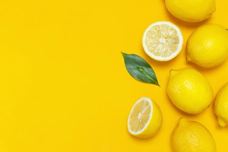 Ripe juicy lemons and green leaves on bright yellow background. Lemon fruit, citrus minimal concept, vitamin C. Creative summer food minimalistic background. Flat lay, top view, copy space.の写真素材