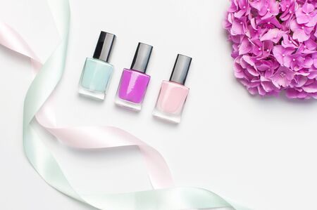 Decorative cosmetics, nail polish. Set of different varnishes for manicure nails on light background with flowers of pink hydrangea top view Flat lay mock up. Female cosmetics. Beauty blogger concept.の写真素材