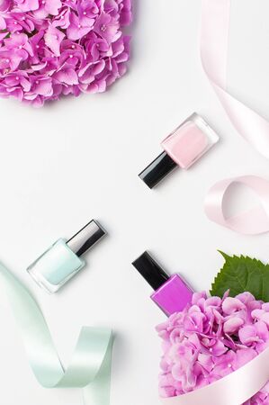 Decorative cosmetics, nail polish. Set of different varnishes for manicure nails on light background with flowers of pink hydrangea top view Flat lay mock up. Female cosmetics. Beauty blogger concept.の写真素材
