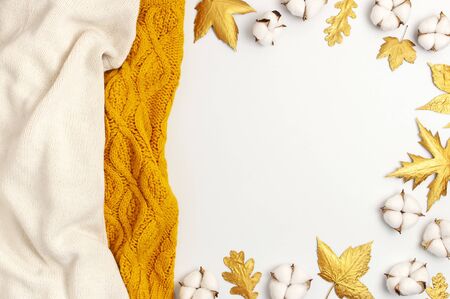 Flat lay autumn composition. Knitted woolen light beige and yellow orange sweater or plaid, golden dry leaves, cotton flowers on white background top view copy space. Autumn, fall concept.の写真素材