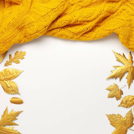 Flat lay autumn composition. Knitted woolen light beige and yellow orange sweater or plaid, golden dry leaves on white background top view copy space. Autumn, fall concept. Knitted texture.の写真素材