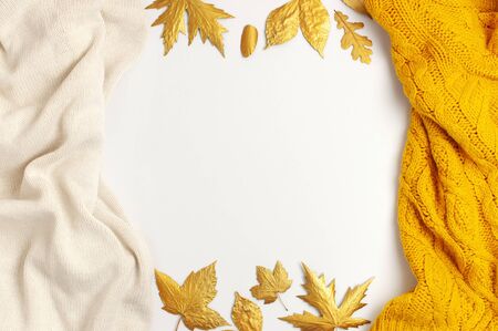 Flat lay autumn composition. Knitted woolen light beige and yellow orange sweater or plaid, golden dry leaves on white background top view copy space. Autumn, fall concept. Knitted texture.の写真素材