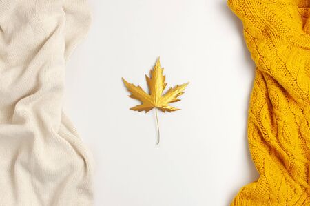 Flat lay autumn composition. Knitted woolen light beige and yellow orange sweater or plaid, golden dry leaves on white background top view copy space. Autumn, fall concept. Knitted texture.の写真素材