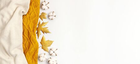 Flat lay autumn composition. Knitted woolen light beige and yellow orange sweater or plaid, golden dry leaves, cotton flowers on white background top view copy space. Autumn, fall concept.の写真素材