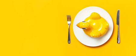 Inflatable mini yellow chicken or duckling on white plate, fork knife on yellow background. Creative food concept, tobacco chicken. Trend Inflatable Children toy for swimming. Layout for design.の写真素材