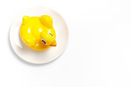 Inflatable mini yellow chicken or duckling on white plate on white background. Creative food concept, tobacco chicken. Flat lay copy space. Trend Inflatable Children toy for swimming Layout for design.の写真素材