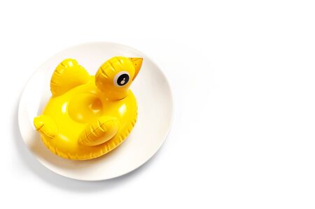 Inflatable mini yellow chicken or duckling on white plate on white background. Creative food concept, tobacco chicken. Flat lay copy space. Trend Inflatable Children toy for swimming Layout for design.の写真素材