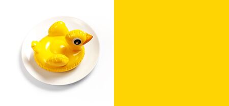 Inflatable mini yellow chicken or duckling on white plate on white background. Creative food concept, tobacco chicken. Flat lay copy space. Trend Inflatable Children toy for swimming Layout for design.の写真素材