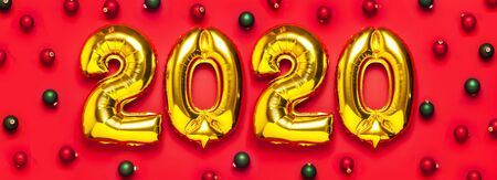 Flat lay 2020 inflatable golden numbers with red and green christmas balls on red background. New year winter decoration, holiday symbol, party item. Merry Christmas greeting card. Happy New Year.の写真素材