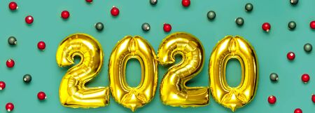 Flat lay 2020 inflatable golden numbers with red and green christmas balls on green background. New year winter decoration, holiday symbol, party item. Merry Christmas greeting card. Happy New Year.の写真素材