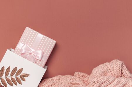 Flat lay autumn composition. Knitted woolen pink female sweater or plaid, pink gift with ribbon, golden dry leaves on burgundy brown background top view copy space. Autumn gift, fall concept.の写真素材