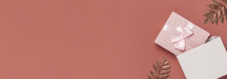 Pink gift or present box with ribbon, golden dry leaves on burgundy brown background top view copy space. Autumn gift, fall concept. Flat lay composition for birthday, mother day, wedding.の写真素材