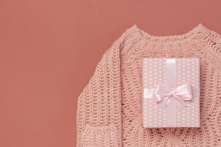 Flat lay autumn composition. Knitted woolen pink female sweater pullover, pink gift with ribbon on burgundy brown background top view copy space. Autumn gift fall concept. Fashionable womens clothing.の写真素材