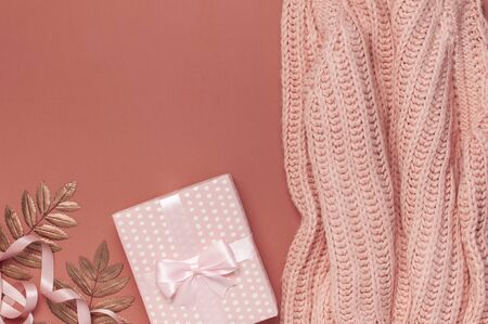 Flat lay autumn composition. Knitted woolen pink female sweater or plaid, pink gift with ribbon, golden dry leaves on burgundy brown background top view copy space. Autumn gift, fall concept.の写真素材