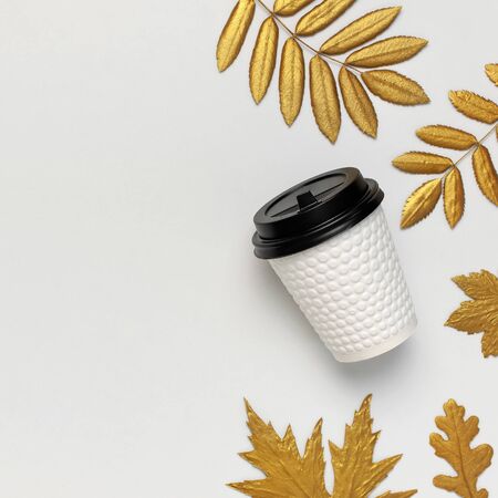 Coffee or tea paper cup, golden autumn leaves on light gray background top view flat lay. Take away coffee cup, mockup. Coffee love, layout for design. Fall concept. Autumn background. Square.の写真素材