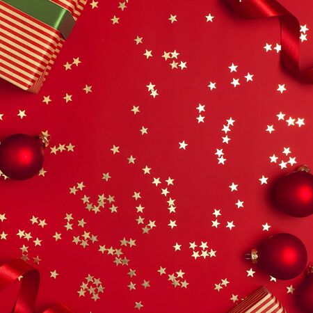 New Year Christmas presents with green ribbon, Christmas balls, gold confetti stars on red background top view. Flat lay Xmas holiday 2020 celebration. Gift boxes greeting card Festive decorations.の写真素材