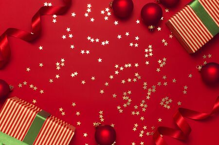 New Year Christmas presents with green ribbon, Christmas balls, gold confetti stars on red background top view. Flat lay Xmas holiday 2020 celebration. Gift boxes greeting card Festive decorations.の写真素材