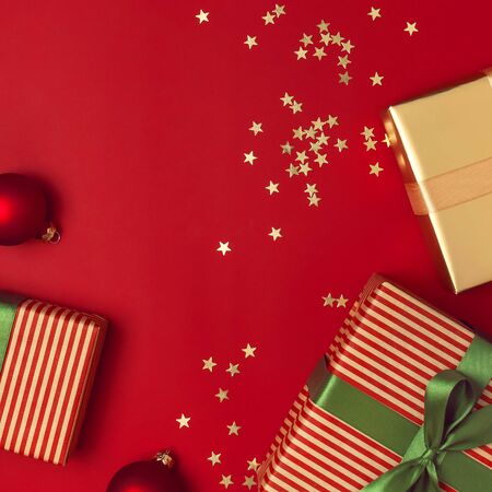 New Year Christmas presents with green ribbon, golden gift, confetti stars on red background top view. Flat lay Xmas holiday 2020 celebration. Gift boxes greeting card Festive decorations.の写真素材