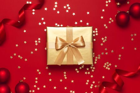 New Year Christmas golden presents with ribbon, Christmas balls, gold confetti stars on red background top view. Flat lay Xmas holiday 2020 celebration. Gift boxes greeting card Festive decorations.の写真素材