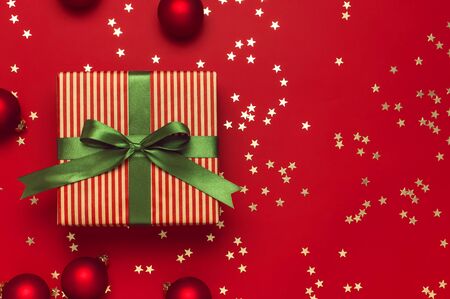 New Year Christmas presents with green ribbon, Christmas balls, gold confetti stars on red background top view. Flat lay Xmas holiday 2020 celebration. Gift boxes greeting card Festive decorations.の写真素材