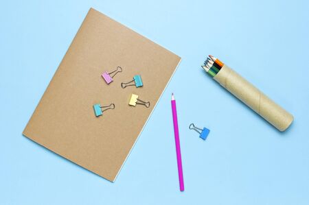 Wooden colored pencils, clean school notebook in line, paper clips on pastel blue background top view flat lay copy space. Pencils for drawing, objects for creativity. Back to school concept.の写真素材
