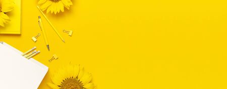Top view flat lay of workspace desk styled design with sunflowers, white paper bag, pencils, pen, paper clips on bright yellow background. Autumn or summer Concept. Sunflower natural background.の写真素材