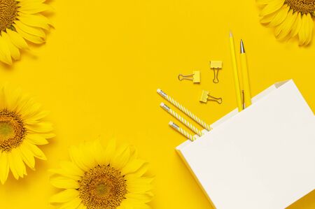 Top view flat lay of workspace desk styled design with sunflowers, white paper bag, pencils, pen, paper clips on bright yellow background. Autumn or summer Concept. Sunflower natural background.の写真素材