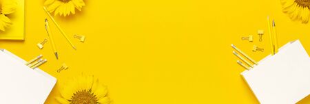 Top view flat lay of workspace desk styled design with sunflowers, white paper bag, pencils, pen, paper clips on bright yellow background. Autumn or summer Concept. Sunflower natural background.の写真素材