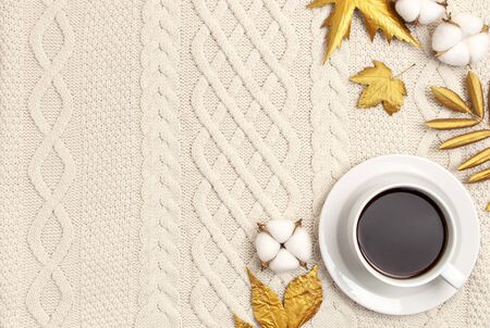 Flat lay autumn composition. Cup of coffee, knitted woolen light beige sweater or plaid, golden dry leaves, cotton flowers top view copy space. Autumn, fall concept. Cozy lifestyle details.の写真素材