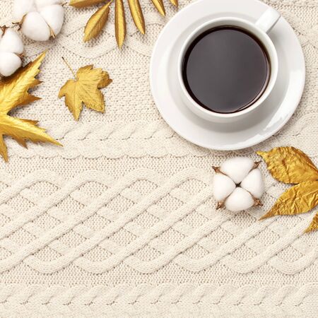Flat lay autumn composition. Cup of coffee, knitted woolen light beige sweater or plaid, golden dry leaves, cotton flowers top view copy space. Autumn, fall concept. Cozy lifestyle details.の写真素材