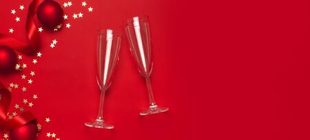 New Year Christmas Champagne glasses, Christmas balls, gold confetti stars on red background top view with copy space. Flat lay Xmas holiday 2020 celebration. Greeting card Festive decorations.の写真素材