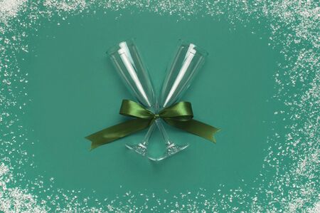 Champagne glasses with festive ribbon on green background with snow top view. Flat lay Xmas holiday 2020 celebration. Creative composition, concept of firework holiday party New Year Christmas.の写真素材
