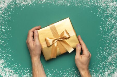 New Year Christmas presents, golden gift in male hands on green background with snow frame top view copy space. Flat lay Xmas holiday 2020 celebration. Gift boxes greeting card Festive decorations.の写真素材
