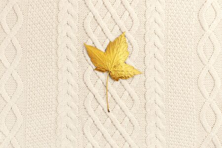 Flat lay autumn composition. Knitted woolen light beige sweater or plaid, golden maple leaf top view copy space. Autumn, fall concept. Cozy lifestyle details.の写真素材