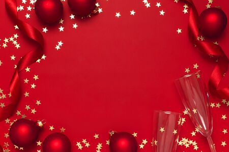 New Year Christmas Champagne glasses, Christmas balls, gold confetti stars on red background top view with copy space. Flat lay Xmas holiday 2020 celebration. Greeting card Festive decorations.の写真素材